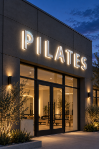 Reverse lit halo channel letters spelling PILATES on a studio at dusk
