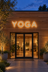 Back lit channel letters spelling YOGA on a wood-clad studio at dusk