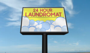 Same laundromat pole sign light box with a backlit banner, seen in daylight