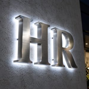 Brushed stainless halo lit channel letters spelling HR on a textured wall
